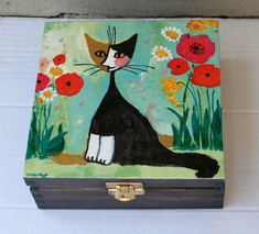 a painted box with a black cat sitting on the ground next to red and white flowers