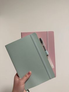 a hand holding a notebook with a pen sticking out of the cover on top of it