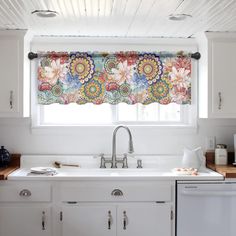 a kitchen with a sink, dishwasher and window covered in colorful floral curtains