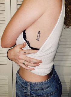 a woman with a small lighthouse tattoo on her left side ribcading the chest