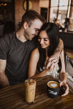 a man and woman sitting next to each other at a table with drinks in front of them