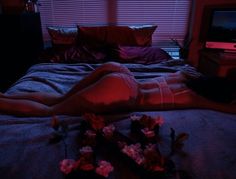 a woman laying on top of a bed next to a window in a room with red lights