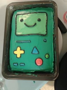 a cake shaped like a gameboy with green frosting and smiling faces on it