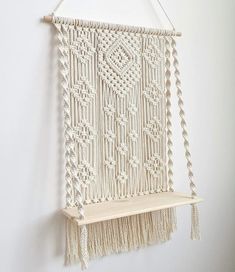 a macrame wall hanging on a white wall next to a shelf with hooks