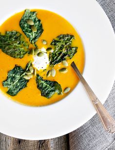 a white plate topped with a yellow soup and spinach garnished in cream