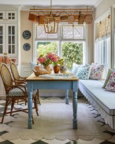 a dining room table and bench with baskets on the windowsill, in front of a checkered floor