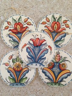 four decorative plates with flowers and leaves painted on them, sitting on a marble surface