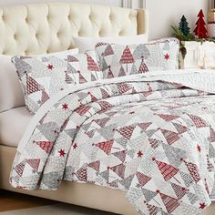 a white bed with red and grey quilts on it in front of a christmas tree