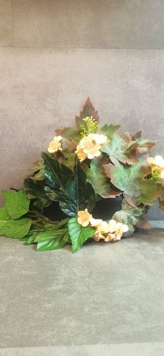 a vase filled with yellow and white flowers on top of a gray countertop next to green leaves