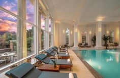 an indoor swimming pool with lounge chairs around it and large windows overlooking the water at sunset