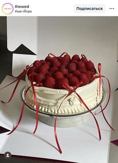 a white cake with raspberries on top and red ribbon around it, sitting on a table