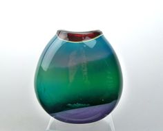 a green and purple vase sitting on top of a wooden stand in front of a white wall