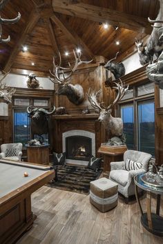 a living room with a pool table and deer heads on the wall over the fireplace