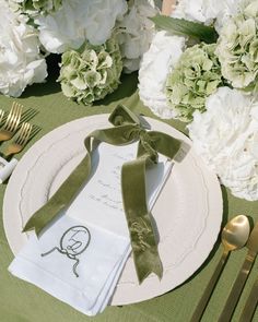 a place setting with white flowers and green napkins, gold forks and silverware