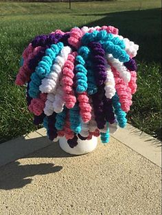 a vase filled with colorful crocheted balls sitting on top of a cement slab