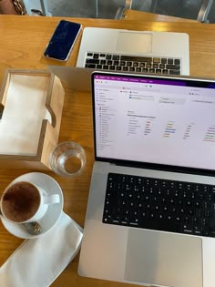 an open laptop computer sitting on top of a wooden table next to a cup of coffee