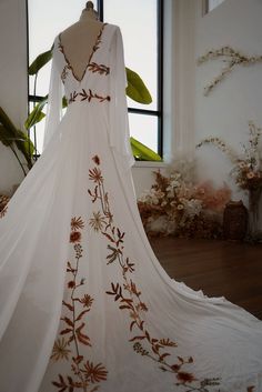 a wedding dress is displayed in front of a large window with flowers on the side