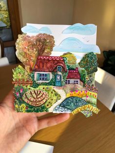 a hand holding up a card with a house on the front and trees in the back