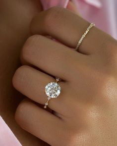 a woman's hand with a diamond ring on top of her finger and a pink flower in the background