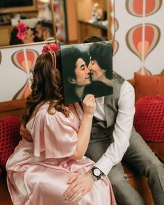 a man and woman sitting next to each other on a couch holding up a photo