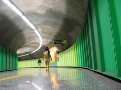 two people are walking through a tunnel with green walls and yellow lines on the floor