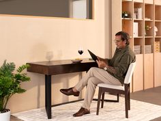 a man sitting at a desk reading a book and holding a glass of red wine