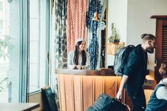 a man and woman are standing in front of a counter with luggage on it, looking out the window