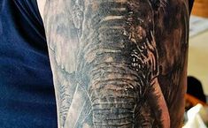 an elephant tattoo on the arm of a man's left arm, with his face partially covered in black and grey ink