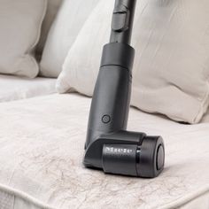 a black and silver vacuum on top of a white bed with pillows in the background