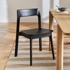 a black chair sitting on top of a wooden floor next to a table and bowl