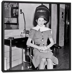 a woman sitting in a chair with a hat on her head and wearing a dress