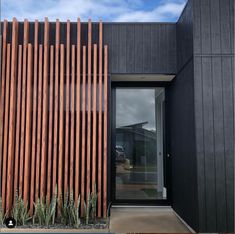 a black building with wooden slats on the side and cactus plants in front of it