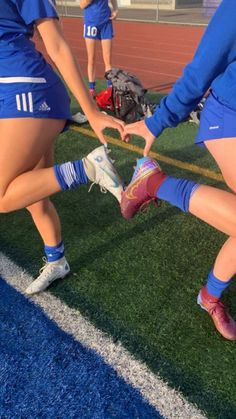 two girls in blue uniforms holding hands on a soccer field