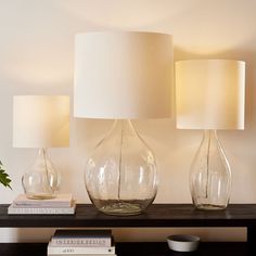 three glass vases sitting on top of a wooden table next to two white lamps