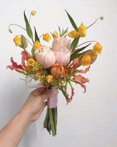 a person holding a bouquet of flowers in front of a white wall with yellow and pink flowers