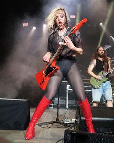 a woman in tights and boots holding a guitar on stage with other people behind her