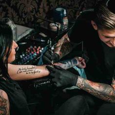 a man getting his tattoo done by a woman in a room with other tattoos on her arm