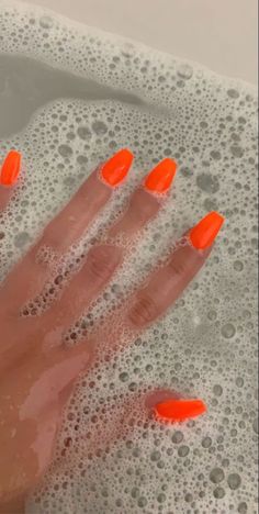 a person's hand with orange nail polish in a bathtub filled with water