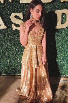 a woman standing in front of a green wall wearing a gold dress and holding her hand up to her face