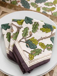 four napkins with green leaves on them sitting on a white plate