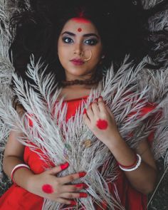 a woman with red makeup and feathers on her head is posing for a photo in the grass