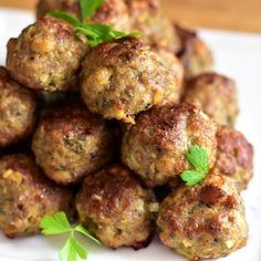 some meatballs are on a white plate and garnished with green leafy herbs