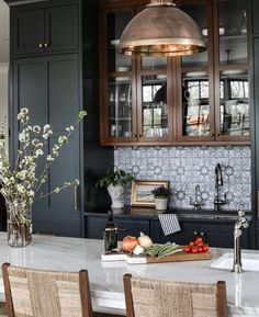 a kitchen with black cabinets and white counter tops, an island sink and a large pendant light hanging over it