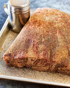 a piece of meat sitting on top of a metal tray next to a salt and pepper shaker