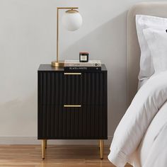 a night stand next to a bed in a room with white walls and wood flooring