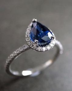 a pear shaped blue sapphire and diamond ring on a gray surface with diamonds around it