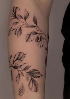 a woman's arm with black and white tattoos on it, showing the leaves