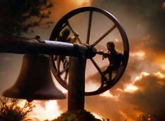 an image of a man on top of a giant bell in front of a cloudy sky