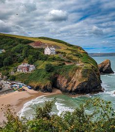 a beach with houses on top of it next to the ocean and green hills in the background