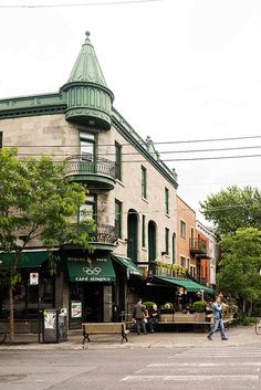 people walking down the street in front of an old building with green awnings